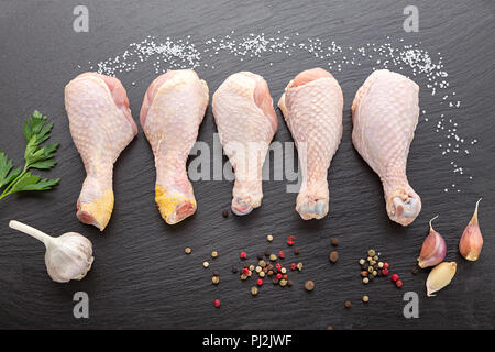 Materie le cosce di pollo rivestito in una riga su sfondo nero con erbe e spezie Foto Stock