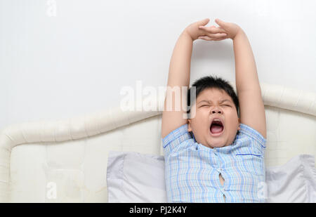 Ragazzo obesi sbadigliare e stretching sul letto in mattinata, il concetto di stile di vita Foto Stock