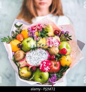 Frutta e bacche bouquet. Mangiare bouquet in mani femminili. Apple, arancia, fragola, pere, kiwi, dragon di frutta e fiori, eucalipto. DOF poco profondo Foto Stock