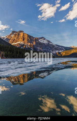 Sebbene il Lago di Smeraldo nel Parco Nazionale di Yoho (Canada) era ancora mezzo ghiacciato, belle riflessioni dell'illuminato montagne emerse al tramonto. Foto Stock