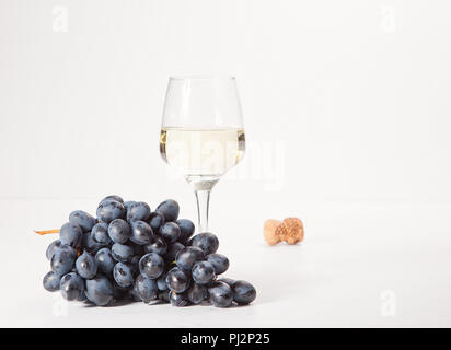 Due bicchieri e una bottiglia di vino bianco su uno sfondo bianco vicino a una manciata di uva Foto Stock