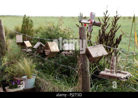 Una fila di graziosi uccelli case appesi ad un filo spinato lungo la strada con un grande vuoto il campo verde in background. Casa in paese! Foto Stock