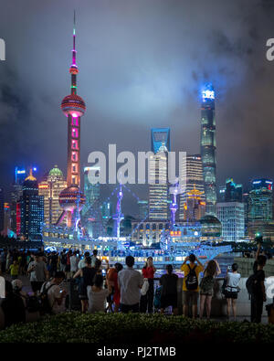 La Folla di cinesi prendere nella Pudong skyline e la torre della Radio di notte mentre la barca vela coperto di luci a LED passa da. Foto Stock