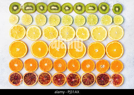 Diverse varietà di agrumi, le arance, i limoni e limette, kiwi disposti in righe. Sfondo colorato, vista dall'alto Foto Stock