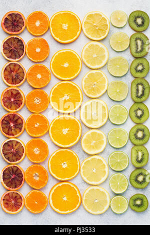 Diverse varietà di agrumi, le arance, i limoni e limette, kiwi disposti in righe. Sfondo colorato, vista dall'alto Foto Stock