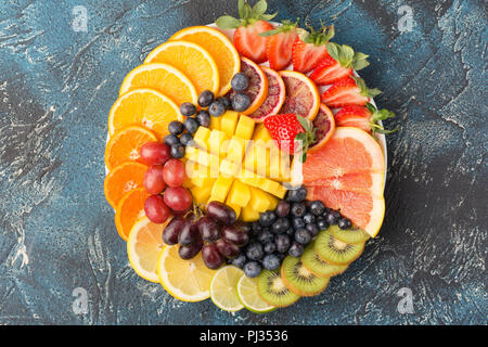 Sani frutti e bacche platter nei colori dell'arcobaleno, fragole, mango, uva, arance e kiwi, limoni sul tavolo blu, copiare lo spazio per testo, il fuoco selettivo Foto Stock