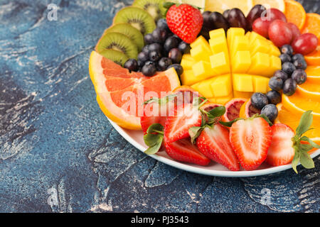 Sani frutti e bacche platter nei colori dell'arcobaleno close up, fragole, mango, uva, arance e kiwi, limoni sul tavolo blu, copiare lo spazio per testo, il fuoco selettivo Foto Stock