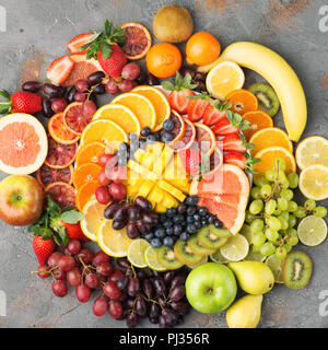 Colorata frutta tagliata platter nei colori dell'arcobaleno Arance Uve mango fragole kiwi mirtilli pompelmo sul cemento grigio tabella disposti in cerchio, vista dall'alto, il fuoco selettivo Foto Stock