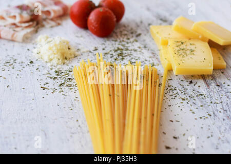 Ingredienti per la cottura- pancetta dolce ciliegie di pomodoro, formaggio, spaghetti-/ di pasta alimentare a sfondo di luce sullo sfondo di legno Foto Stock