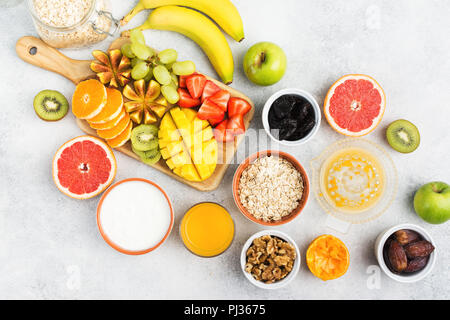 Sana colazione con fiocchi d'avena, varietà di frutti, fragole, mango, uva, fichi, yogurt e noci servita al tavolo bianco, sopra il fuoco selettivo Foto Stock