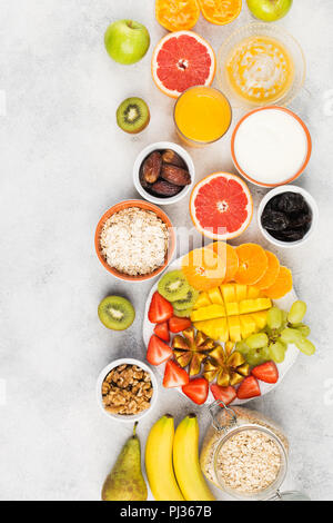 Vista dall'alto di una sana colazione con fiocchi d'avena, varietà di frutti, fragole, mango, uva, servita al tavolo bianco, copiare lo spazio per testo, selettivo foc Foto Stock