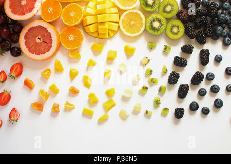 Vista aerea di frutti interi e tagliare a fette in righe, rosso, arancione, giallo, verde di frutta con pezzi tagliati sullo sfondo bianco, succo di pompelmo, mango Foto Stock