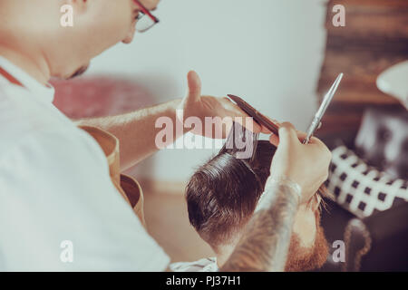 Barbiere taglia la tipologia dei capelli del cliente nel suo negozio di barbiere. Foto in stile vintage Foto Stock