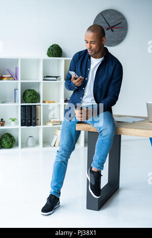 Felice African American businessman utilizzando un telefono cellulare in un ufficio. Foto Stock