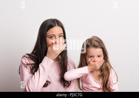 Una piccola ragazza e sua madre in un monolocale, mani sulla loro bocca. Foto Stock