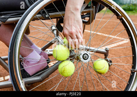 Disabilitato giovane donna sulla sedia a rotelle giocando a tennis sui campi da tennis. Close-up di una mano tiene una palla da tennis fissato in una ruota Foto Stock