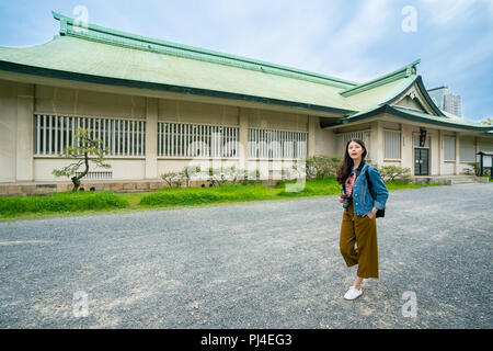 Rilassata visitatore asiatici a piedi lungo il sentiero di fronte all'edificio nel castello di Osaka con il blu del cielo. Foto Stock