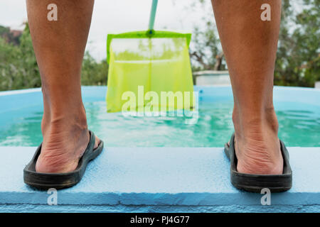 Primo piano di un giovane uomo caucasico, visto da dietro la pulizia delle acque di una piscina con una foglia skimmer montato in un palo telescopico Foto Stock