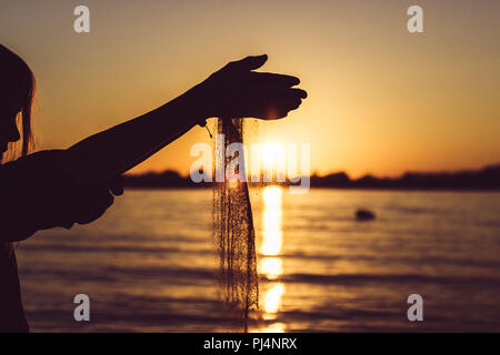 Donna che gioca con la sabbia sulla spiaggia con tramonto Foto Stock