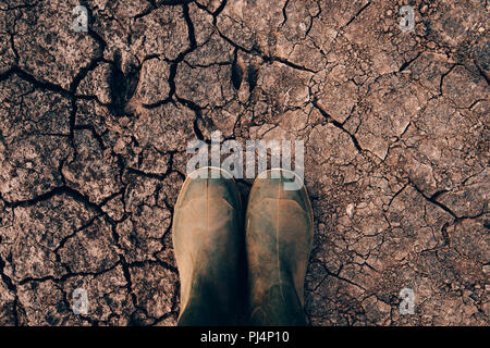 Agricoltore in stivali di gomma in piedi sul suolo asciutto terra, il riscaldamento globale e i cambiamenti climatici influiscono sulle colture e la resa Foto Stock