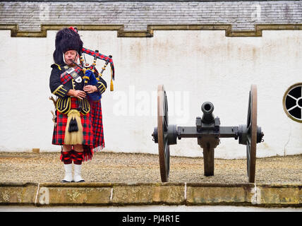 La Scozia, Perthshire, Blair Castle, Piper nel tradizionale abito scozzese giocando la cornamusa accanto a un cannone al castello. Foto Stock