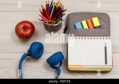 Forniture scolastiche. Le cuffie Apple, un supporto in metallo per matite con matite di colore, aprire il quaderno sul sacchetto custodia a matita con colore pennarelli e un marcatore Foto Stock