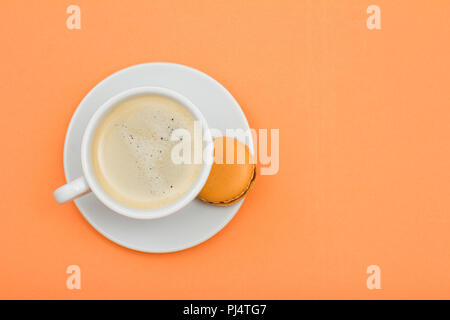 Porcellana Bianca tazza di caffè e una deliziosa torta macaron sul piattino con pesca sfondo colorato. Vista superiore Foto Stock