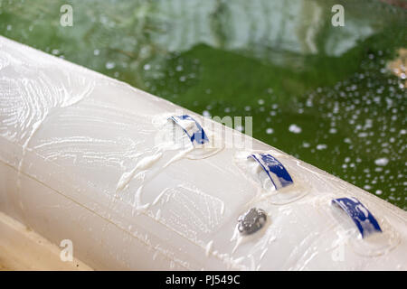 L'uomo bianco lavaggio barca gonfiabile con pennello e con acqua in pressione sistema a garage. Servizio nave e stagionali e un concetto di manutenzione. Foto Stock