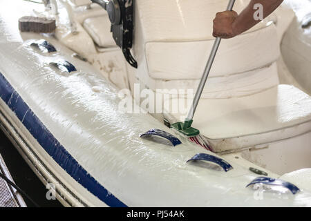 L'uomo bianco lavaggio barca gonfiabile con pennello e con acqua in pressione sistema a garage. Servizio nave e stagionali e un concetto di manutenzione. Foto Stock