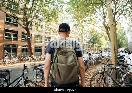 Uno studente con uno zaino o un turista su strada di Lipsia in Germania nei pressi del parcheggio per biciclette che si trova accanto alla biblioteca dell'Università di Leipig e ostello della gioventù. Foto Stock