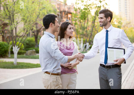 Felice coppia giovane stringono le mani con fiduciosa imprenditore Foto Stock