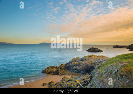 Arty, sunset seascape guardando fuori dalle rocce su Ynys Llanddwyn (isola di marea in Anglesey N.Galles) verso Yr Eifl (i rivali in inglese). Incredibile cielo Foto Stock