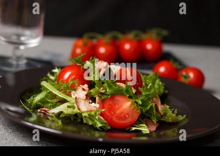 Pomodori ciliegia e lattuga mescolati in insalata su piastra nera Foto Stock