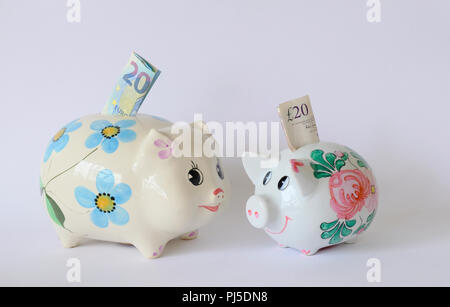 Coppia di cina piggy banche più grandi con un 20 Euro nota e la più piccola con una 20 pound nota Foto Stock