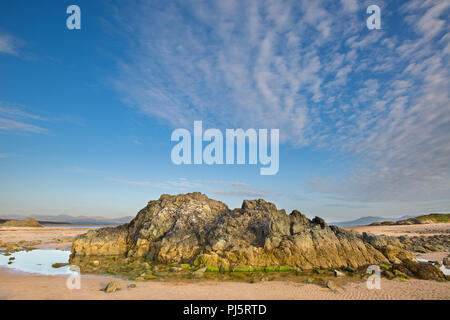 Spiaggia vuota, Ynys Llanddwyn (isola di marea, Anglesey, Galles) con grandi rocce scoscese & piscine di roccia. Cielo blu e wispy cirrus nubi atmosferiche sulla costa. Foto Stock