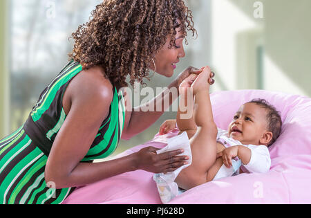Igiene bambino. Vista laterale verticale di un felice Afrriican, American, madre cambiando pannolino per bambino Foto Stock