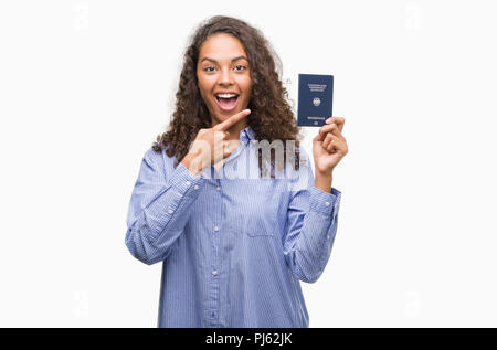 Giovane donna ispanica tenendo il passaporto della Germania molto felice puntando con mani e dita Foto Stock