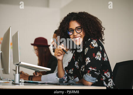 Sorridente imprenditrice tenendo la penna digitale seduto alla sua scrivania assieme ai suoi colleghi in ufficio. Imprenditrice utilizzando un blocco di scrittura digitale e penna Foto Stock