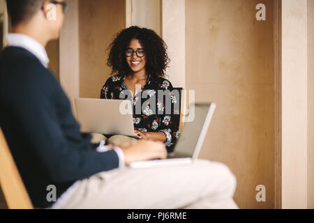 Donna sorridente imprenditore lavora su laptop seduti su una sedia con un imprenditore seduto davanti. Ufficio colleghi operanti su notebook seduto su cha Foto Stock