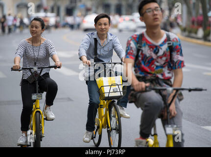 Persone a cavallo delle biciclette per le strade di Shanghai in Cina Foto Stock