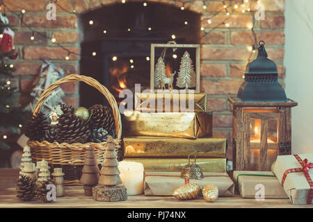 Scuro composizione Natale lanterna, presenta artigianali e decorazioni in legno sul tavolo davanti al camino con woodburner, ornamenti e garlan Foto Stock