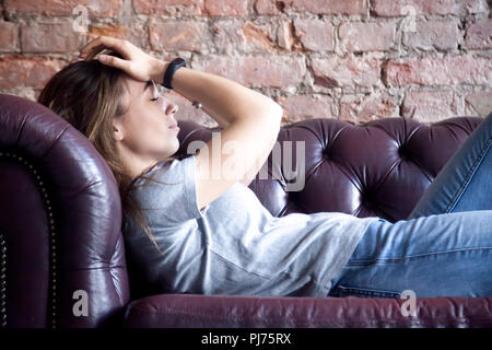 Triste e ragazza disperata rivolta verso crisi risiede sul lettino tenendo la testa con le mani Foto Stock