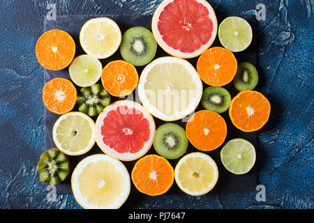 Frutta Ricca di vitamina C: arance, limoni, kiwi, pompelmi e limette in ardesia nera su sfondo blu scuro, vista dall'alto Foto Stock