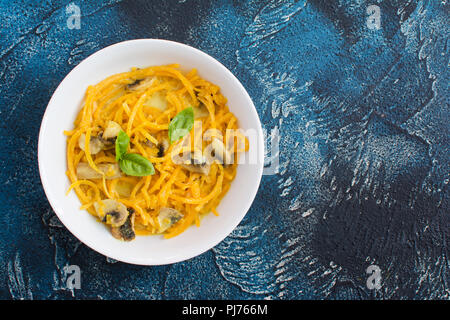 Vista superiore della spiralizzato zucca pasta fatta con il latte di cocco,salsa al curry e musrooms, blu sul tavolo di pietra, il fuoco selettivo, copia spazio per te Foto Stock