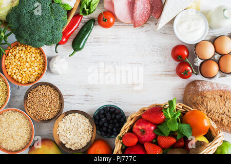 Varietà di frutta e verdura, cereali, prosciutto, formaggio, uova, pane sul bianco tavolo in legno, vista dall'alto, copia spazio, selecitve focus. Cesto di strawb Foto Stock