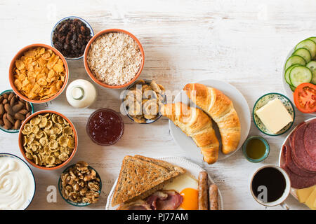 Vista superiore del riempimento di una sana prima colazione, uova, salsicce, pancetta, fagioli, formaggio, cereali, toast, dadi, marmellate, ortaggi, croissant, il fuoco selettivo Foto Stock