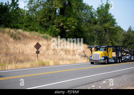 Specializzata giallo vuota big rig car hauler semi carrello con due-tiered semi rimorchio andando a caricare le vetture su strada tortuosa con hill e alberi verdi Foto Stock