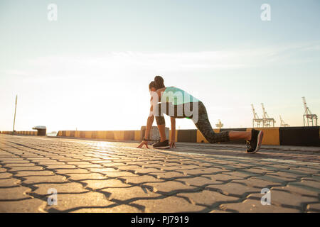 Montare e fiducioso della donna nella posizione di partenza pronta per l'esecuzione. Atleta femminile circa per avviare una volata che guarda lontano. Foto Stock