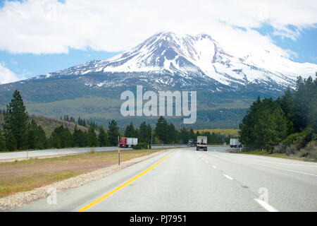 Un multi-lane highway road con un setto di prato e di linea con big rig semi carrelli con diversi semirimorchi in movimento in entrambe le direzioni e un molto bello Foto Stock