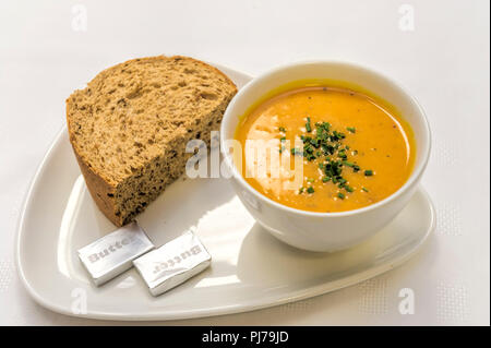 In casa la Zucca minestra con erbe aromatiche spruzzata sulla sommità servita con una spessa fetta di pane su una piastra bianca con sfondo bianco Foto Stock